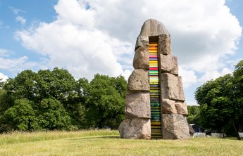 Kunst & Kultur (© MHT.SH & Peter Lühr) Bunte Steinskulptur auf einer grünen Wiese.