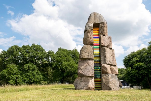 Kunst & Kultur (© MHT.SH & Peter Lühr) Bunte Steinskulptur auf einer grünen Wiese.