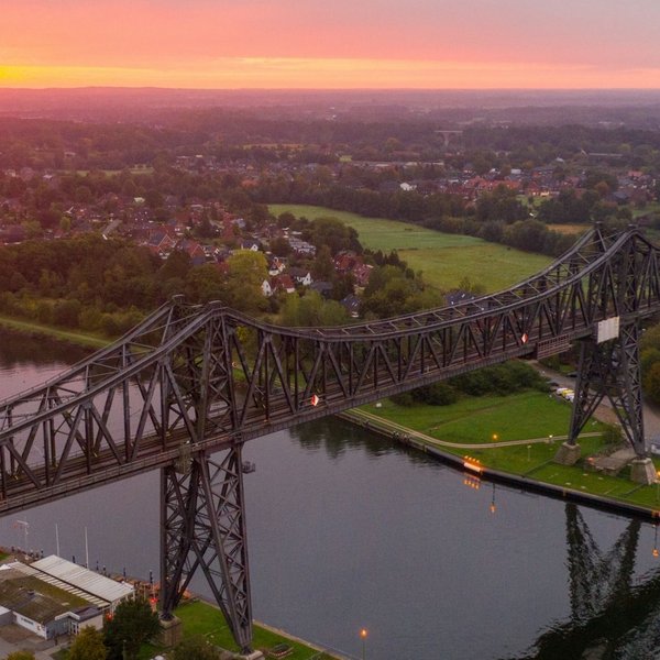 (© sh-tourismus.de / MOCANOX) Luftaufnahme der Rendsburger Hochbrücke und des Nord-Ostsee-Kanals bei Sonnenuntergang