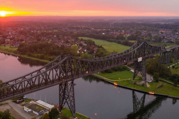 (© sh-tourismus.de / MOCANOX) Luftaufnahme der Rendsburger Hochbrücke und des Nord-Ostsee-Kanals bei Sonnenuntergang