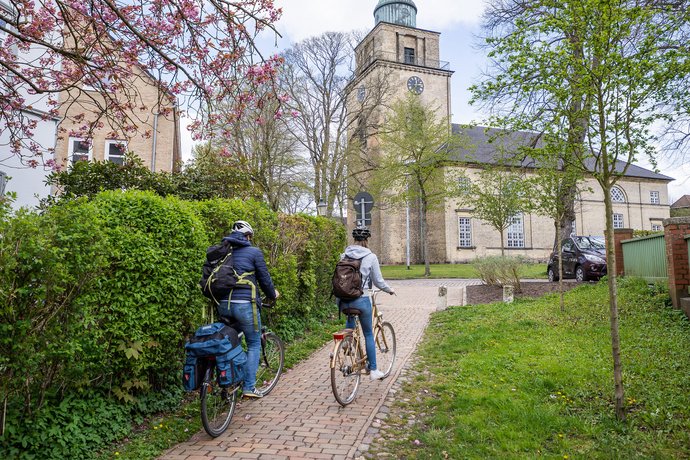 Ausflugstipps (© sh-tourismus.de/MOCANOX) Zwei Radfahrer fahren im Frühling auf eine Kirche zu.